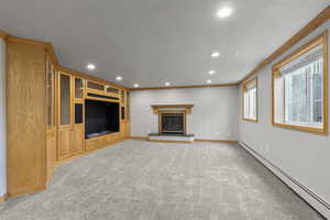 Unfurnished living room featuring a baseboard heating unit, crown molding, recessed lighting, light carpet, and a glass covered fireplace