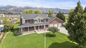 Back of house with covered porch, a lawn, a shingled roof, driveway, and a mountain view
