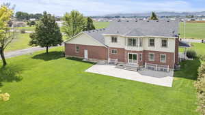 Rear view of property featuring brick siding, a yard, roof with shingles, a patio, and a mountain view
