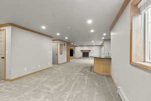Unfurnished living room with ornamental molding, baseboard heating, recessed lighting, a fireplace with raised hearth, and light carpet