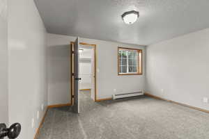 Unfurnished bedroom with carpet, a walk in closet, a textured ceiling, and a baseboard radiator
