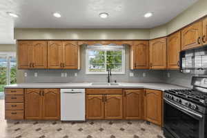Kitchen featuring stainless steel gas range, light countertops, black microwave, dishwasher, and brown cabinets