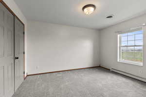 Unfurnished bedroom featuring a closet, carpet flooring, and a baseboard heating unit