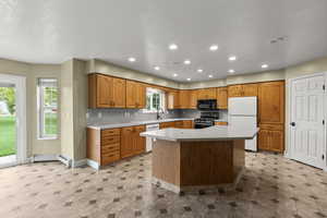 Kitchen featuring white appliances, a kitchen island, light countertops, brown cabinetry, and recessed lighting
