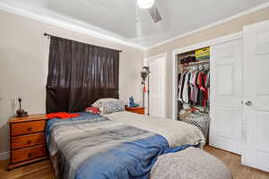 Bedroom featuring light wood-style flooring, a closet, crown molding, and a ceiling fan