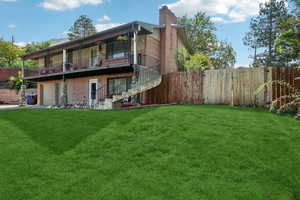 Rear view of house featuring brick siding, a balcony, a chimney, stairway, and a garage