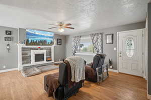 Living area with wood finished floors, a textured ceiling, a fireplace, and a ceiling fan