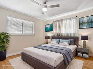 Bedroom with light wood-style floors, ornamental molding, and a ceiling fan