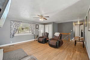 Living area with an upstairs landing, light wood finished floors, a textured ceiling, and ceiling fan
