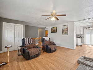Sitting room featuring a textured ceiling, light wood-style floors, a ceiling fan, arched walkways, and an upstairs landing