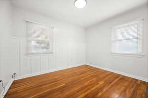 Empty room with wood finished floors, wainscoting, and a decorative wall