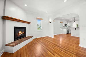 Unfurnished living room featuring arched walkways, healthy amount of natural light, recessed lighting, light wood finished floors, and a glass covered fireplace