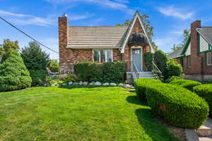 English style home featuring brick siding, a front yard, a tiled roof, and a chimney