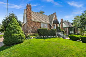 Tudor-style house with brick siding, a front lawn, and a chimney