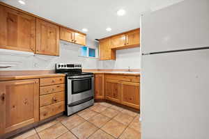 Kitchen with freestanding refrigerator, stainless steel electric range oven, light countertops, light tile patterned floors, and recessed lighting