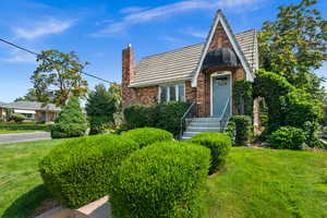 Tudor home with brick siding, a front lawn, and a chimney