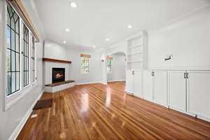 Unfurnished living room with arched walkways, light wood finished floors, recessed lighting, and a glass covered fireplace