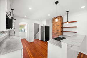 Kitchen featuring white cabinets, freestanding refrigerator, hanging light fixtures, open shelves, and arched walkways