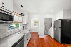 Kitchen featuring appliances with stainless steel finishes, light stone countertops, white cabinets, dark wood finished floors, and healthy amount of natural light