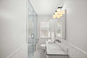 Full bathroom featuring tile walls, a wainscoted wall, vanity, a shower stall, and light tile patterned floors