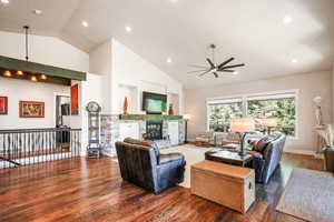 Living room with dark wood-type flooring, recessed lighting, high vaulted ceiling, ceiling fan, and a stone fireplace