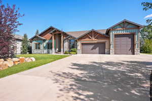 Craftsman inspired home featuring concrete driveway, an attached garage, stone siding, a front yard, and board and batten siding