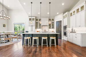 Kitchen featuring white cabinetry, glass insert cabinets, a kitchen bar, a large island, and backsplash