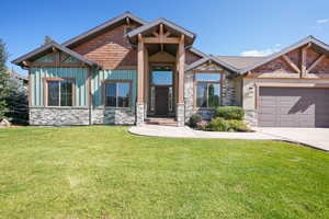Craftsman inspired home featuring stone siding, a front yard, board and batten siding, and an attached garage
