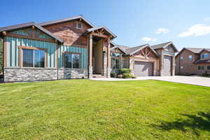 Craftsman house featuring stone siding, board and batten siding, a front yard, and concrete driveway