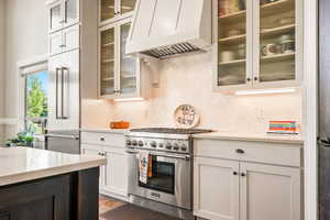 Kitchen featuring high quality appliances, premium range hood, white cabinetry, beverage cooler, and light stone counters