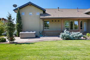 Rear view of property with a hot tub, a yard, a shingled roof, stucco siding, and covered porch