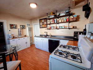 Kitchen featuring white range with gas cooktop, light wood-style flooring, white cabinetry, a heating unit, and dark countertops