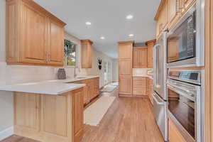 Kitchen featuring stainless steel appliances, tasteful backsplash, light wood-style floors, a peninsula, and light brown cabinetry