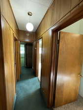 Corridor featuring dark colored carpet and wooden walls