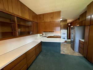 Kitchen with brown cabinets, light countertops, open shelves, freestanding refrigerator, and a peninsula