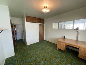 Home office with a textured ceiling and dark colored carpet
