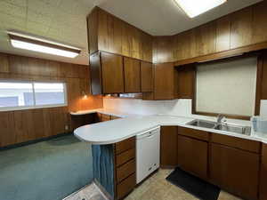 Kitchen with wooden walls, light countertops, light carpet, white dishwasher, and a peninsula
