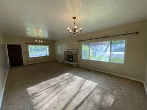 Unfurnished living room featuring a chandelier, a fireplace, carpet flooring, and a textured ceiling