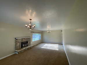Unfurnished living room with a chandelier, a fireplace, a textured ceiling, and carpet floors