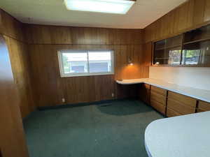 Kitchen with brown cabinets, dark colored carpet, wood walls, and light countertops