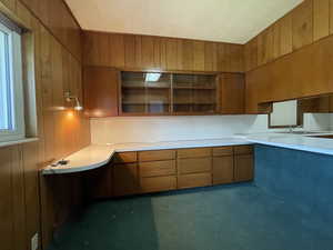 Kitchen with brown cabinetry, wood walls, and light countertops