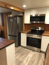 Kitchen with wooden counters, stainless steel appliances, white cabinetry, light wood finished floors, and wooden walls