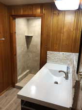 Bathroom featuring wooden walls, vanity, light wood-type flooring, and a tile shower