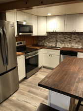 Kitchen with butcher block counters, white cabinets, appliances with stainless steel finishes, and tasteful backsplash