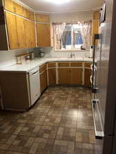 Kitchen featuring brick patterned flooring, freestanding refrigerator, light countertops, dishwasher, and brown cabinetry