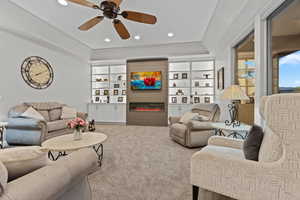 Living area featuring a tray ceiling, a glass covered fireplace, recessed lighting, a ceiling fan, and carpet
