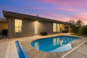 Back of property at dusk with a patio area, an outdoor pool, stucco siding, and a tile roof