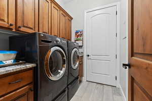 Washroom featuring light wood-style flooring, washing machine and clothes dryer, and cabinet space