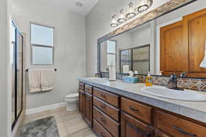 Full bath featuring a stall shower, double vanity, light wood-style floors, and tasteful backsplash