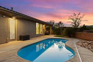 Pool at dusk with a fenced backyard and a patio area
